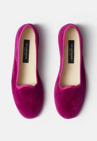 Zapatos de ante fucsia tipo slip-on con punta redonda y una textura suave. El interior cuenta con un forro beige y una etiqueta de marca visible.