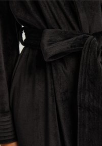 Svart morgonrock i mjukt, plyschigt material. Har ett knytbälte och ribbat accent på ärmen som visar en jämn, texturerad yta.