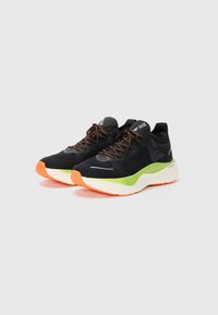 Black athletic shoes with green and white midsoles, orange soles, and black laces with orange accents on a white background.