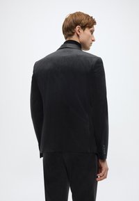 Schwarze Anzugjacke aus glattem Stoff, mit klassischem Schnitt, einfachem Schlitz und dezenten Knopfdetails an den Ärmeln.