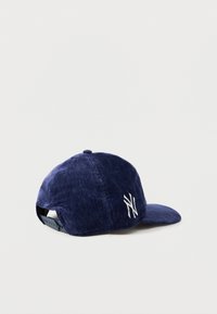 Navy velvet baseball cap with a curved brim and white embroidered logo on the side. Adjustable strap at the back for sizing.