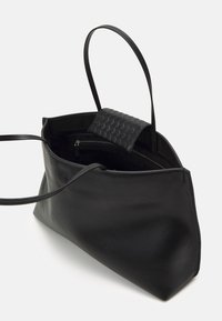 Borsa tote in pelle nera con manici lunghi e una tasca trapuntata testurizzata. Presenta un vano interno con zip e una superficie esterna liscia.