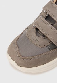 Baskets grises avec un mélange de suède et de mesh texturé, fermeture à double sangle, et semelle en caoutchouc à détails en grille.