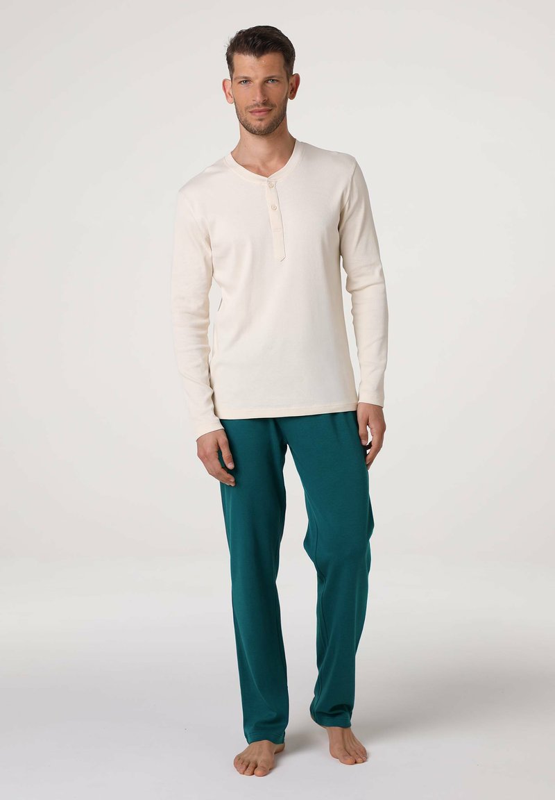 Maglietta henley crema a maniche lunghe con tre bottoni abbinata a pantaloni turchese; entrambi in tessuto morbido e liscio.