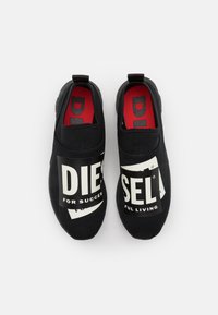 Musta liukusasennettavat tennarit, joissa on suuret valkoiset logo-tekstit "DIESEL FOR SUCCESS" ja "FUL LIVING". Sisällä punaiset pohjat ja teksturoitu kangas päällinen.