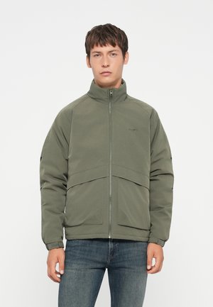 Olive green jacket with high collar, front zipper, and two large front pockets. Features a smooth, matte texture and contrasting seams.