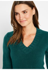 Maglione lavorato a maglia color teal con scollatura a V e colletto a coste. Texture morbida e maniche lunghe, aderente al corpo.