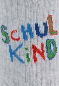 Szara wełniana skarpetka z napisem "SchulKind" w kolorowej haftowanej czcionce: niebieskie, czerwone, zielone i pomarańczowe litery o teksturowanym wykończeniu.