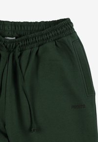 Ciemnozielone spodnie dresowe z elastycznym paskiem w talii i regulowanym sznurkiem. Posiada boczne kieszenie oraz małe czarne logo z przodu.