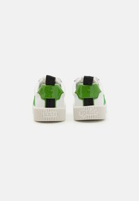 Sneakers bianche con dettagli in pelle verniciata verde e suola in gomma strutturata. Presentano linguette nere e il marchio "kate spade" in rilievo.