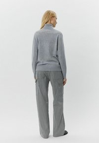 Pelēks adīts augstais kakls džemperis ar brīvu piegriezumu, kombinēts ar platām svītrainām biksēm ar kargo kabatām. Mīksta tekstūra un daudzfunkcionāls dizains.