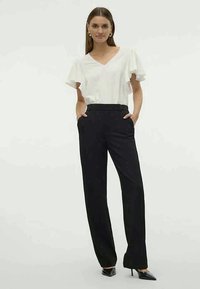 Weißes V-Ausschnitt-Blusenshirt mit kurzen Rüschensäumen, kombiniert mit hochtaillierten schwarzen Hosen mit Seitentaschen und geradem Bein.