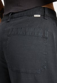 Dark denim pants featuring a back pocket with subtle texturing. A small brand label is visible near the waistband.