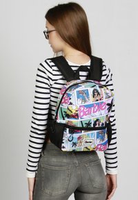 La mochila presenta un estampado de Barbie multicolor y de estilo caricaturesco, un gran compartimiento principal y detalles de malla negra en la parte frontal y lateral.