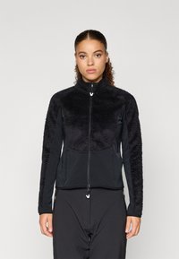 Musthave mustan riidejope, millel on pehme karvane tekstuur ülemises osas ja sile kangas varrukatel. Omab kõrget kraed ja kahte küljetaskut.