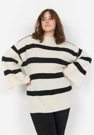 Cream and black striped sweater with a loose fit, wide sleeves, and ribbed texture. Crew neckline. Paired with black pants.