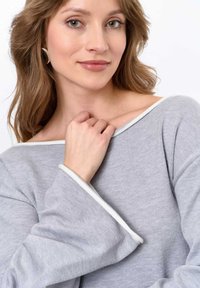 Gray ribbed sweater featuring a wide neckline and white trim. Model is touching her collar, with soft waves in her hair.