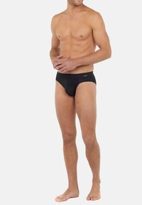 Schwarze Boxershorts aus glattem Material mit elastischem Bund und enger Passform, getragen von einem männlichen Modell, das leicht zur Seite geneigt ist.