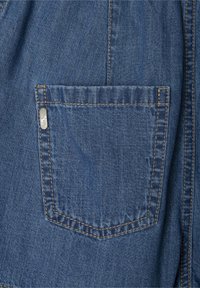 Denim audums vidēji zilos toņos ar vienu aizmugurējo kabatu, kas izceļas ar kontrastējošām oranžām šuvēm un nelielu metāla tagu. Auduma tekstūra ir gluda.
