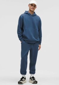 Set di felpa con cappuccio e pantaloni della tuta in tessuto blu profondo, con tasca frontale e vita regolabile, abbinato a scarpe da ginnastica nere e bianche.
