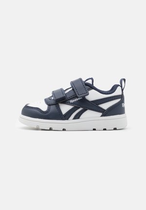 Baskets enfant blanches et bleu marine Reebok avec deux bandes velcro et semelle en caoutchouc, montrées en profil latéral sur un fond neutre.