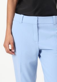 Light blue tailored trousers with a smooth texture, flat front, belt loops, and a side pocket, paired with a black top.