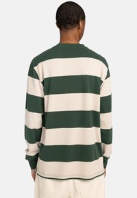 Long-sleeve shirt with alternating green and beige stripes, cotton material, relaxed fit, crew neck, and side slit details.