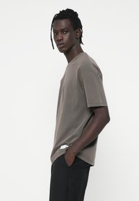 Kortærmet, taupe bomulds T-shirt med rund halsudskæring og subtile syninger. Den har et mærke nær kanten.