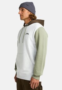 Hoodie met een grijs en bruin kleurblokken ontwerp, voorzien van een kangoeroezak en ribgebreide boorden. De stof voelt zacht aan.