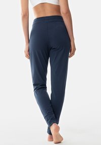 Pantalones de tela elástica azul marino con una textura suave, cintura elástica y perneras ajustadas, mostrados desde la parte trasera con los pies descalzos.
