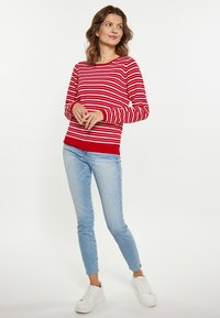 Pulover cu maneci lungi, în dungi roșii și albe, cu guler rotund, asortat cu blugi skinny de culoare bleu deschis și teniși albi.