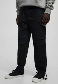 Czarne spodnie cargo wykonane z wytrzymałej bawełny o luźnym kroju, z wieloma kieszeniami i sznurkiem w talii, w połączeniu z czarnymi sneakersami.