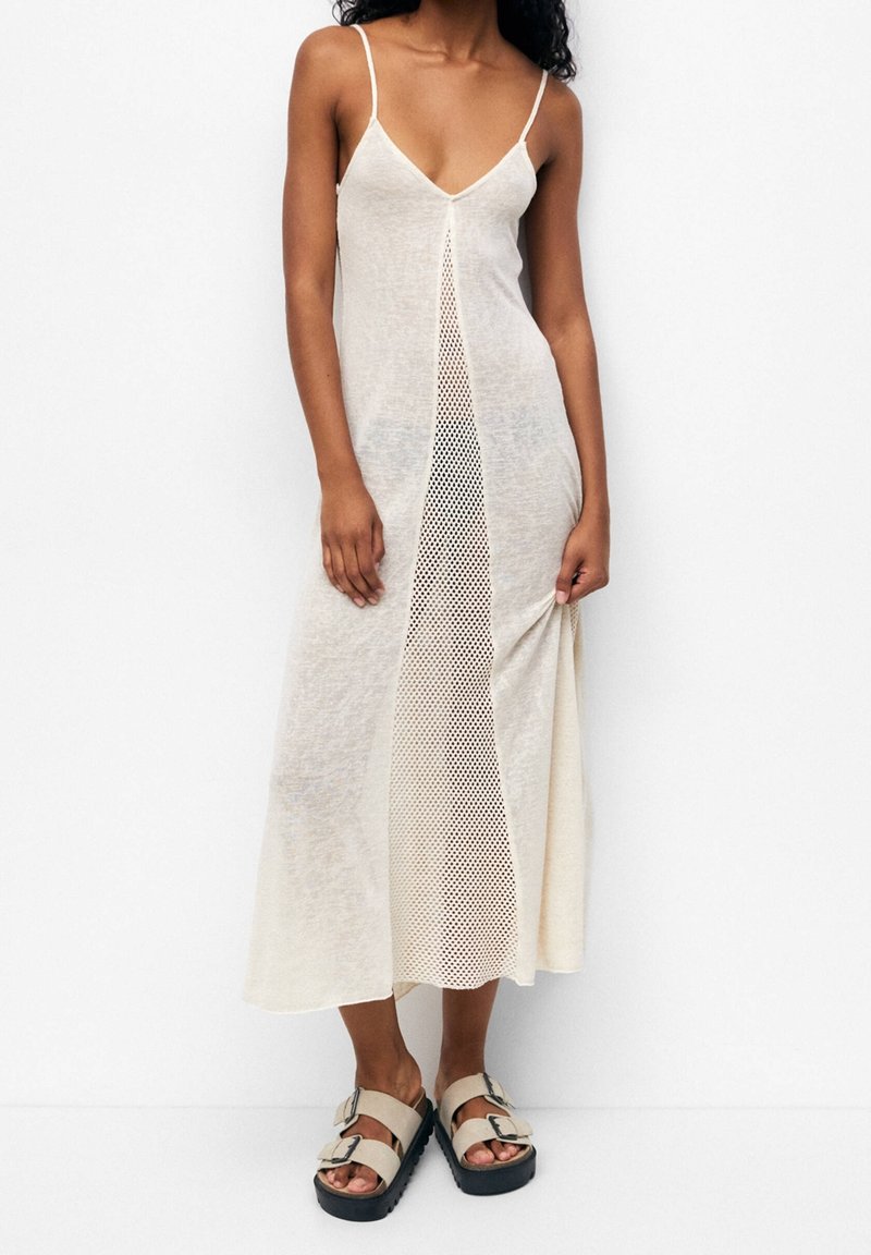 Robe maxi beige clair avec décolleté en V et fines bretelles, dotée d'un panneau en mesh central. Associée à des sandales beiges à plateforme noire.
