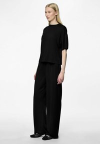 Maglia nera, comoda e a maniche corte, abbinata a pantaloni neri a gamba larga. Texture morbida e design minimalista. Indossato con calzature nere.