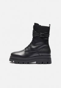 Botte cheville en cuir noir avec un bout arrondi, un laçage à l'avant, un détail de boucle sur le côté et une semelle en caoutchouc épaisse.
