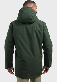 Dunkelgrüne, wasserdichte Jacke mit Kapuze, ausgestattet mit einem Reißverschluss, langen Ärmeln und einer glatten Textur. Die Rückansicht zeigt ein schlichtes Design ohne sichtbare Logos.