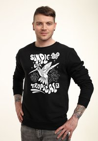 Sort sweatshirt med hvid grafisk design, der inkluderer tekst og en kolibri omgivet af blomsterelementer. Glat stof med ribbestrikkede manchetter.