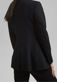 Czarna marynarka z wyraźnymi ramionami, dopasowanym krojem i rozcięciem z tyłu. Gładki materiał z ozdobnym guzikiem na rękawach.