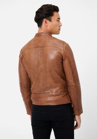 Brun læderjakke med en tætsiddende design, glat tekstur og minimale syningsdetaljer, båret over sorte bukser.