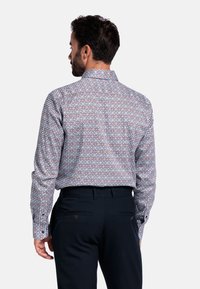 Langarmshirt met een geometrisch patroon in rood, blauw en wit, voorzien van een gestructureerde kraag en knoopmanchetten. Donkere broek zichtbaar.