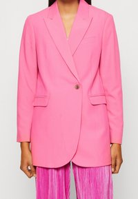 Růžový blazer s klopovým límcem, jedním knoflíkem, dvěma předními kapsami a přiléhavým střihem. Hladká látka s matným povrchem.