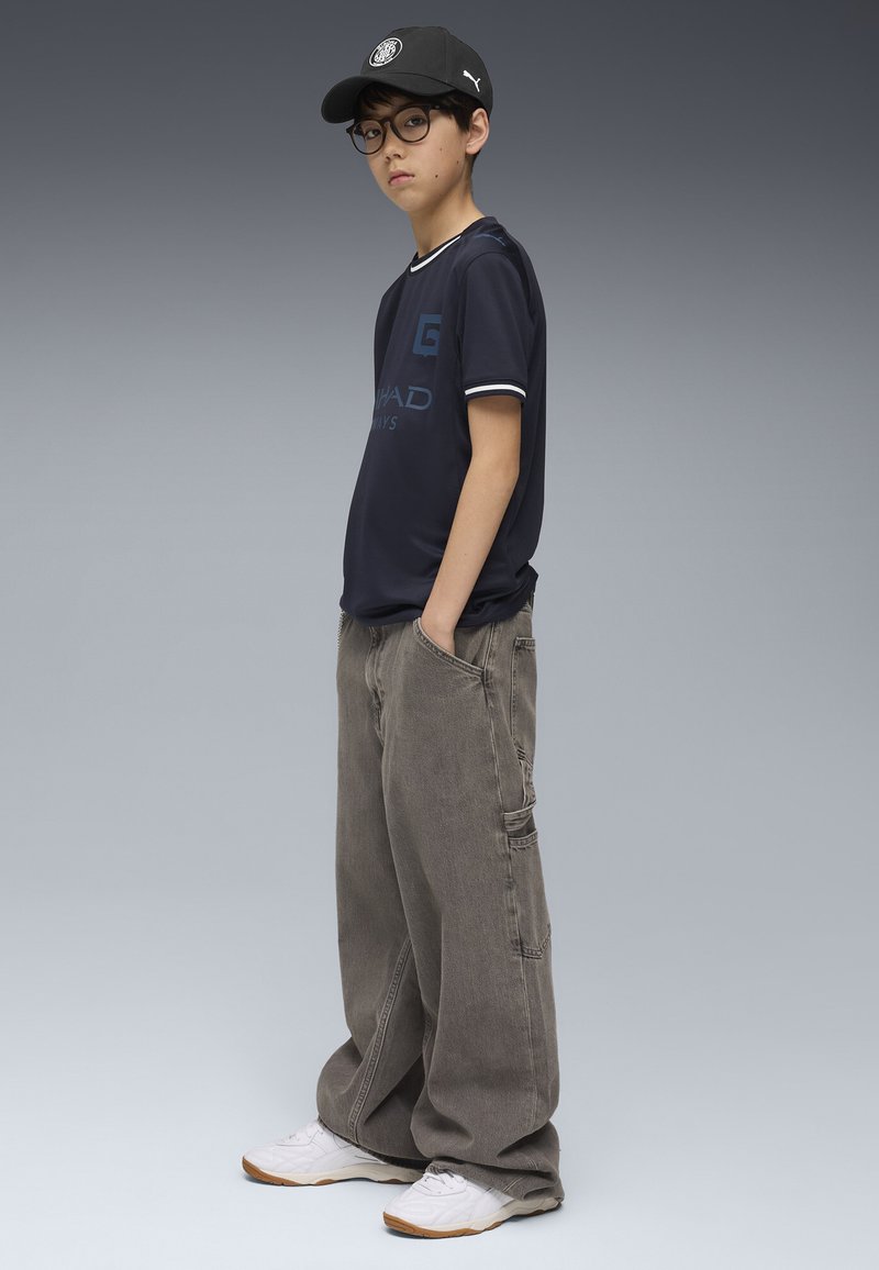 T-shirt i marineblå med hvid kant, cargo grå bukser og hvide sneakers. Accessories inkluderer en sort kasket og runde briller.