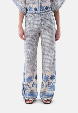 Pantaloni a gamba larga con motivo botanico blu e bordo smerlato, vita con coulisse, indossati con top abbinato e sandali con punta aperta.