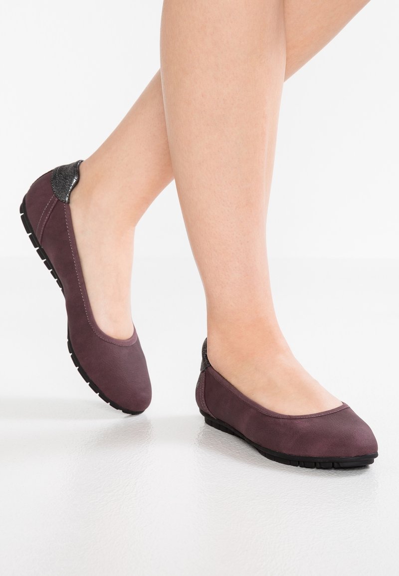 Chaussures plates violettes avec un bout arrondi, une tige en matériau lisse et des accents texturés noirs au niveau du talon. Semelle en caoutchouc avec motifs antidérapants.