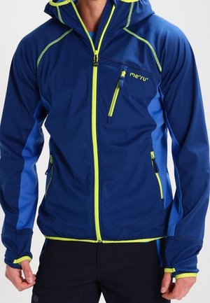Man draagt een blauwe en neon groene softshell jas met capuchon en ritssluitingen in de zakken, staand tegen een effen achtergrond.