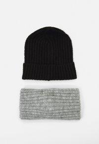 Beanie a coste nera sopra una fascia per la testa a coste grigia chiara; entrambi gli oggetti mostrano una morbida texture e un design casual.