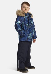 Vinterjacka i blått med abstrakt mönster, utrustad med foder i päls, dragkedjestängning och elastiska ärmslut. Kombineras med mörka byxor och stövlar.