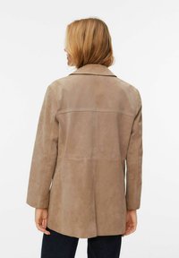 Veste en daim beige avec un col classique, des manches longues et un ourlet droit. Présente une texture lisse et un design minimaliste.