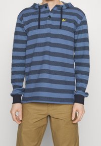 Blå och marinrandig långärmad hoodie med knappad hals, ribbad mudd, och en liten gul logotyp på bröstet. Tillverkad av bomullsblandning.