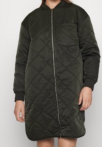 Pikowany, sięgający do kolan płaszcz w ciemnozielonym kolorze z przednim zamkiem błyskawicznym, ściągaczami na mankietach i boczną kieszenią. Gładka faktura i wzór w romby.